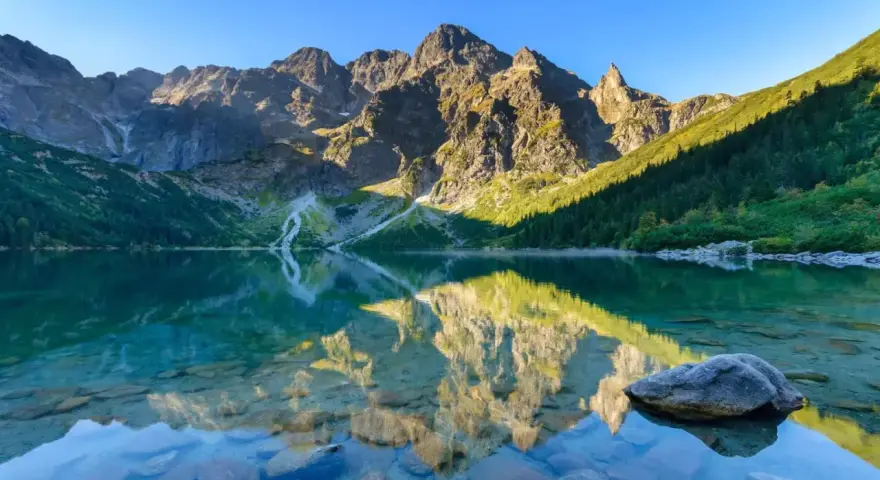 Spokojne jezioro odbija skaliste szczyty. Woda jest krystalicznie czysta, widać kamienie na dnie. To właśnie tutaj, gdzie są Tatry, natura zachwyca.