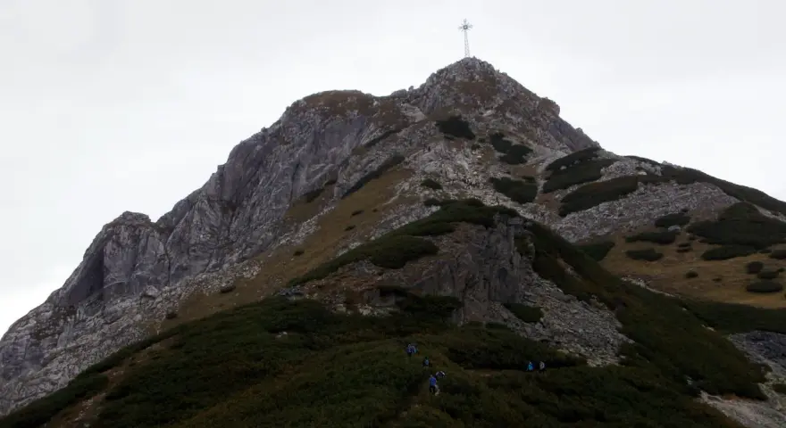 Grupa turystów podąża szlakiem na Giewont. W oddali widać charakterystyczny krzyż na szczycie.