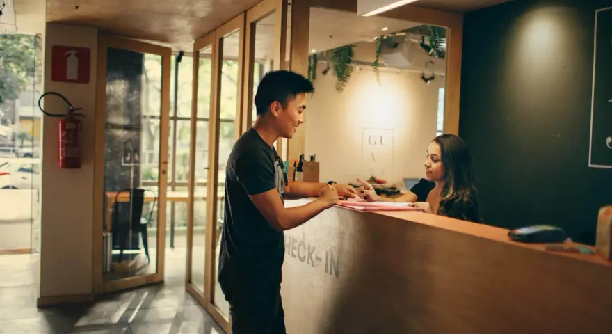 Mężczyzna melduje się w hotelu. Pracownica recepcji wyjaśnia, ile zarabiają turcy w hotelach, gdy obsługuje gościa.