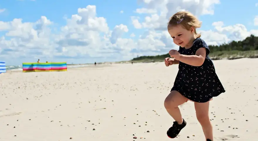 Radosna dziewczynka biega po piaszczystej plaży. Wspaniałe wakacje na Słowacji z dziećmi to marzenie każdego rodzica.