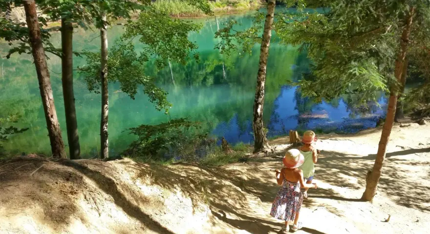 Dwie dziewczynki w słomkowych kapeluszach idą ścieżką nad turkusowe jezioro. Idealne miejsce na wycieczkę w jakie gory z dziecmi.
