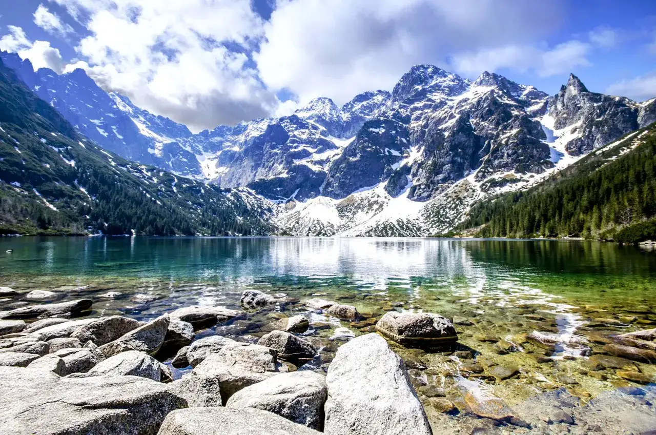 Morskie Oko, jedne z najpiękniejszych gór w Polsce, lśni w słońcu. Skaliste dno jeziora, turkusowa woda i ośnieżone szczyty Tatr tworzą zapierający dech w piersiach widok.