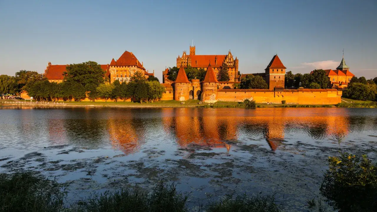 Zamek w Malborku, wpisany na listę UNESCO Polska, odbija się w spokojnej wodzie rzeki Nogat.
