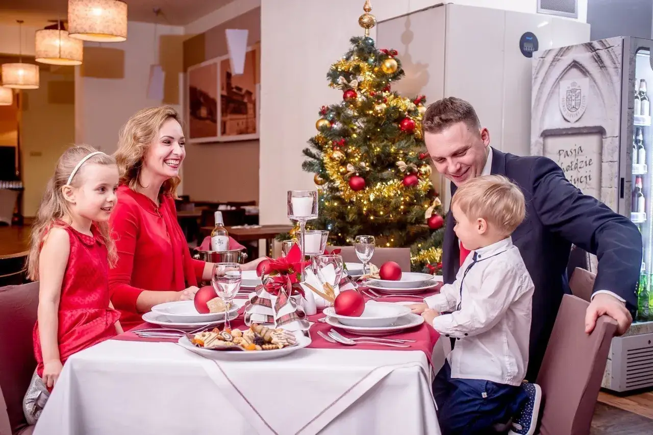 Rodzina celebruje wigilię w hotelu przy choince. Uśmiechnięci rodzice i dzieci zasiadają do uroczystej kolacji.