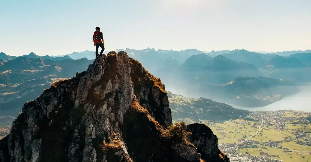 Alpinista na szczycie góry, podziwiający panoramę. Nawet najtrudniejsze momenty wspinaczki prowadzą do takich widoków.
