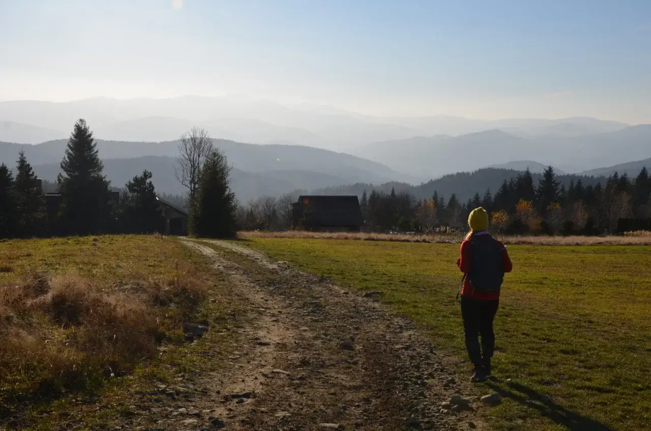 Widok na pasmo górskie z koskową górą w tle. Turystka z plecakiem podziwia krajobraz.