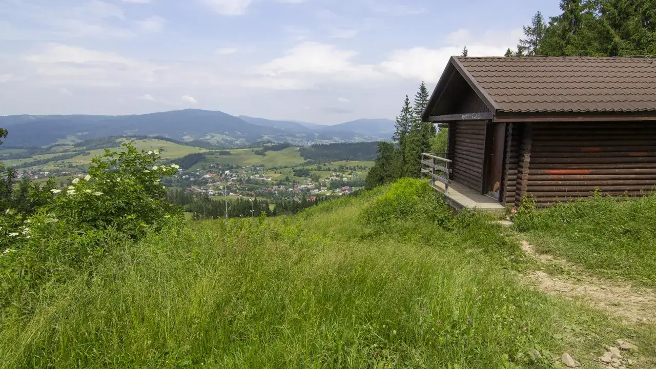 Drewniana chata na szlaku Maciejowa z widokiem na dolinę i góry.