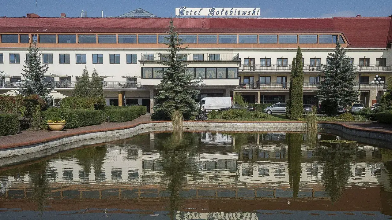 Hotel Gołębiewski, z charakterystycznym napisem na dachu, otoczony zielenią i stawem z odbiciem, to miejsce, które może być najstarszy hotel Gołębiewski.