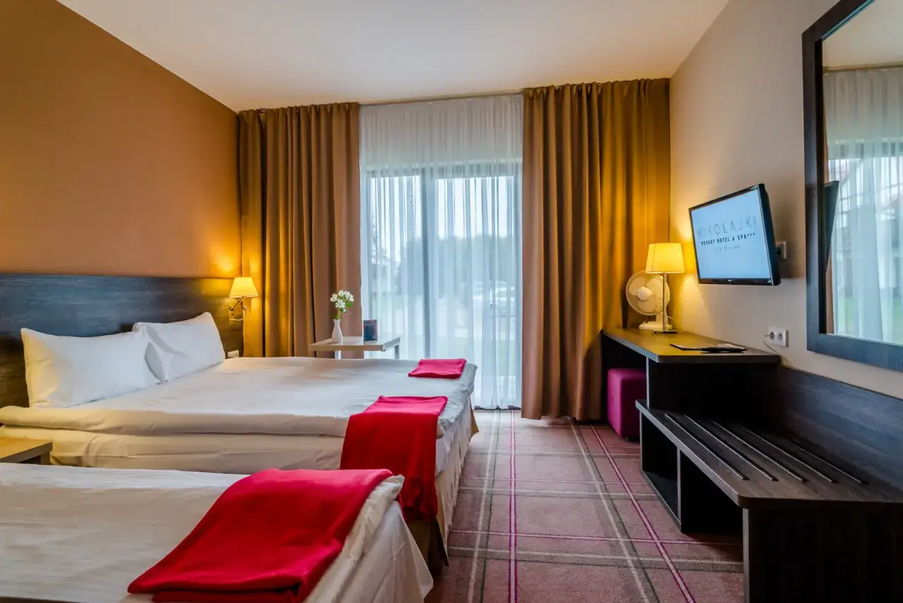 Pokój w Mikołajki Resort Hotel & Spa z dwoma łóżkami, czerwonymi pledami i widokiem na ogród.