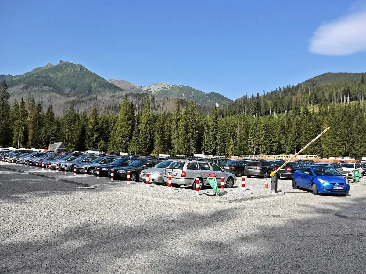 Parking przy Morskim Oku. Kamera rejestruje szlaban i zaparkowane samochody na tle gór i lasu.